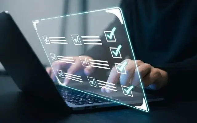 Manos escribiendo en una laptop detrás de una interfaz flotante con una lista de verificación armada.