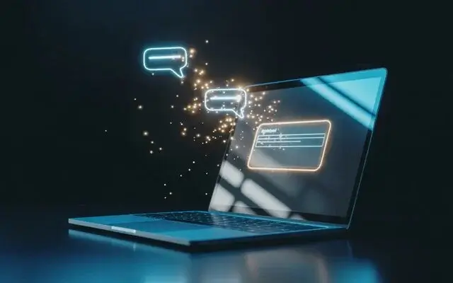 Computadora portátil abierta con globos de diálogo holográficos y partículas de luz flotantes.